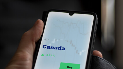 An investor's analyzing the Canada etf fund on screen. A phone shows the ETF's prices marché canadien market canada canadian to invest