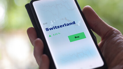 An investor's analyzing the Switzerland etf fund on screen. A phone shows the ETF's prices switzerland etf to invest in Swiss market