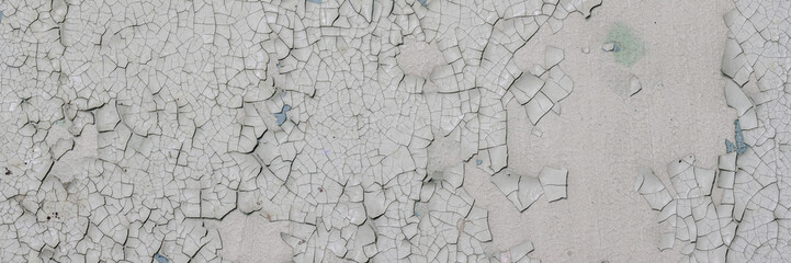 Peeling paint on the wall. Panorama of a concrete wall with old cracked flaking paint. Weathered rough painted surface with patterns of cracks and peeling. Wide panoramic grungy texture for background