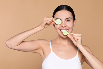 Beautiful young woman with slices of cucumber on beige background