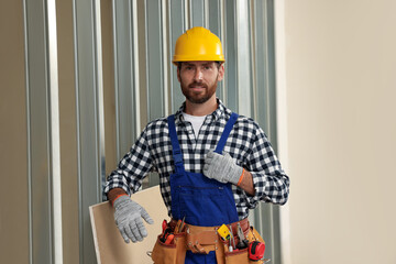 Professional builder in uniform with tool belt indoors