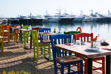 Beautiful view of outdoor cafe with colorful wooden chairs near pier