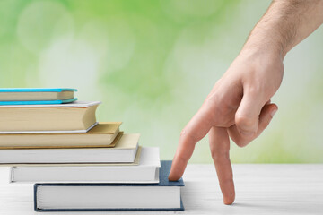 Man climbing up stairs of books with fingers on white wooden table against blurred background, closeup
