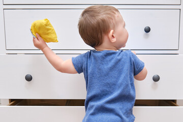 Toddler baby opens a chest of drawers. Child boy reaches into an open drawer of a white cabinet. Kid age one year