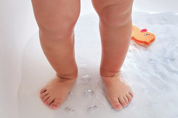 Toddler baby legs is standing on a non-slip mat in the bathtub. Child boy foots washes on the anti...