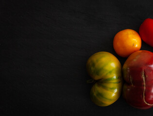 four colorful  organic heirloom Tomatoes on a black stone background,  green, red, yellow, orange
