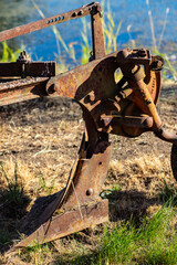 This is a digitally enhanced image of an antique, rusty plow with brown grass and blue water in the background.