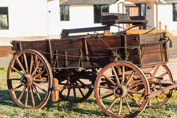 Fototapeta na wymiar This is a digitally enhanced, color image of a buck board wagon. The evening sunlight accentuates the textures as well as the orange and brown colors. Out-of-focus home is in the background