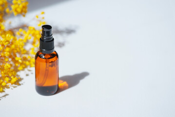Amber pump bottle with serum, tonic or essential oil with yellow flowers. White background with daylight. Beauty concept for face and body care