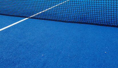 View of the net and the centre line of a blue paddle tennis court.