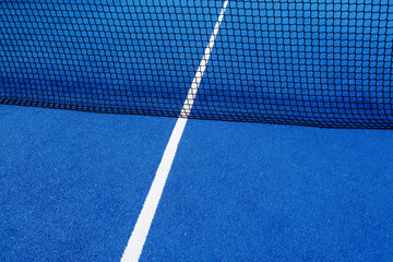 View of the net and the centre line of a blue paddle tennis court. Racket sports