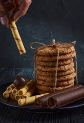 Various cookies and sweets lie on a dark dish. In the left corner of the frame is a hand with a cookie. Vertical frame orientation.