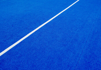 View of the net and the centre line of a blue paddle tennis court. Racket sports