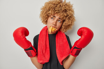 Upset tired female boxer has mouth full of fries keeps arms raised wears black t shirt red towel...