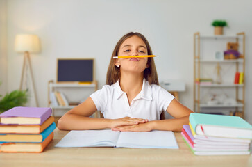 Portrait of funny and positive schoolgirl who at home having fun while doing school homework. Girl...