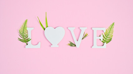 Love letters with green leaves decorated on pastel pink background. Flat lay