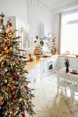 Christmas atmosphere on white Scandinavian kitchen with large windows, decorated with Christmas trees with garland lights and red toys. Empty space