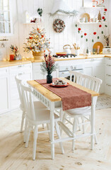 Wooden dining table with white chairs on blurred background of scandinavian kitchen decorated for christmas.