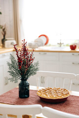 A fresh ruddy Christmas cake is cooling down on a table against a blurred background of a Scandinavian kitchen interior decorated for Christmas.