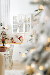 Light Scandinavian kitchen interior with Christmas decorations. Selective focus, view through a blurred Christmas tree with bokeh from the lights of the garlands
