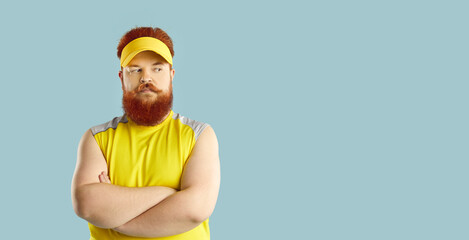 Thoughtful fat athlete standing with arms crossed isolated on blue copyspace background. Plump sportsman looking at copy space on the right and thinking. Chubby guy questioning his workout results