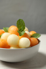 Melon balls and mint in bowl on white wooden table, closeup