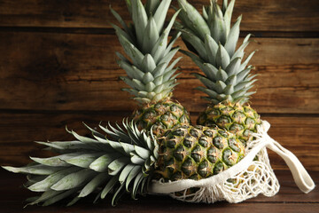 Bag with fresh juicy pineapples on wooden table, closeup