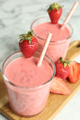 Tasty strawberry smoothies in glasses on wooden board, closeup