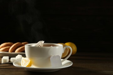 Tea bag in ceramic cup of hot water and lemon on dark wooden table. Space for text