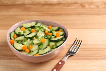 Tasty fresh salad with cucumber in bowl and fork on wooden table