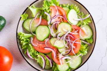 Salad of cucumbers, tomatoes and onions on lettuce on a plate. Vegetarian food. Top view. Closeup
