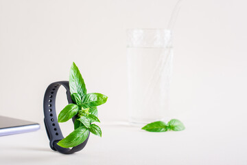 Fresh leaves on the screen of a fitness bracelet, smartphone and a glass of water. The concept of health care, vitality