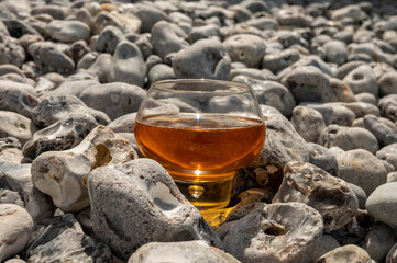 Glass of apple cider drink and stones on pebbles beach of Etretat, Normandy, France