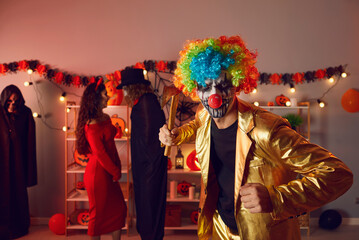 Young guy in costume of spooky evil clown at Halloween party with friends. Adult man wearing golden...