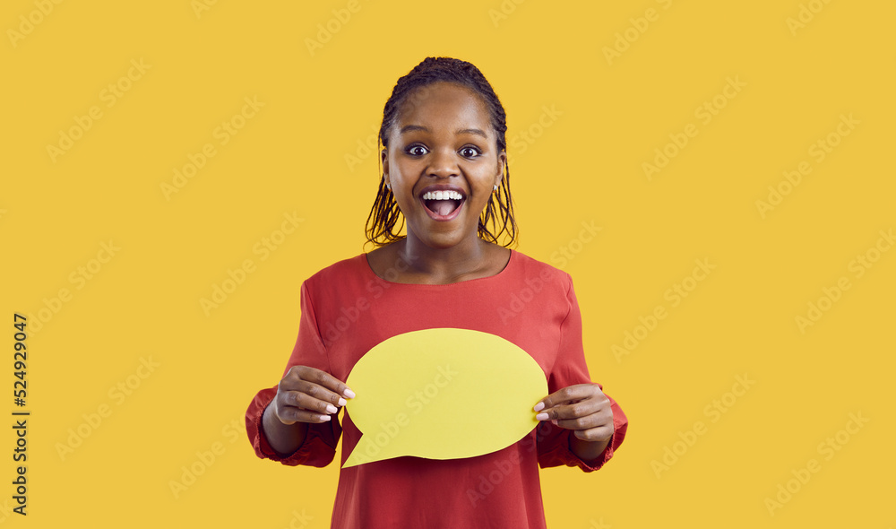 Wall mural Studio shot of happy black woman with speech bubble. Afro American lady with funny excited face expression holding mock up copyspace speech balloon standing isolated on yellow color background