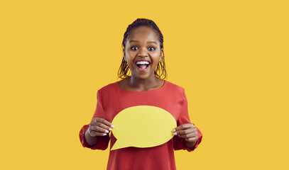 Studio shot of happy black woman with speech bubble. Afro American lady with funny excited face expression holding mock up copyspace speech balloon standing isolated on yellow color background
