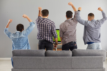 Four young men supporting their favourite team while watching live football game on television at...