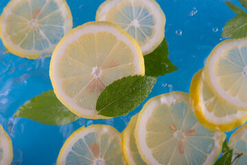Round lemon slices falling deeply under water with green mint leaves on blue background. Selective...