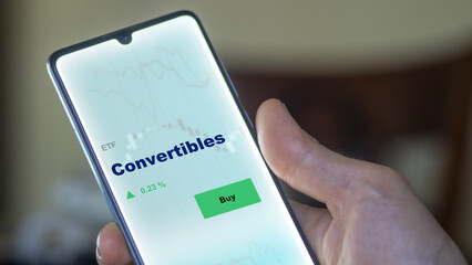 An investor's analyzing the convertibles etf fund on screen. A phone shows the ETF's prices stocks to invest