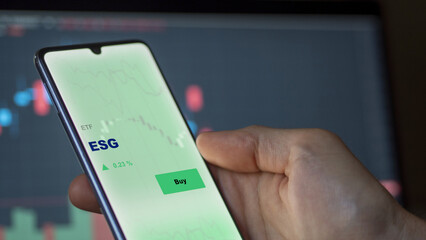 An investor's analyzing the ESG etf fund on screen. A phone shows the ETF's prices esg to invest