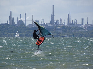 Windsurfing foil boarder flying out of water in choppy seas,  sailing boats and sea traffic in the...