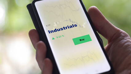 An investor's analyzing the industrials etf fund on screen. A phone shows the ETF's prices stocks to invest
