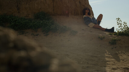 Carefree girl sitting shadow leaning on hill. Attractive woman relax on sand.