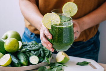Female hands hold a glass of freshly made green smoothie, selective focus, copy space. Vegetarianism