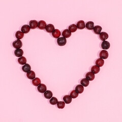Hearg shape made with red cherries on pastel pink background with copy space. Flat lay