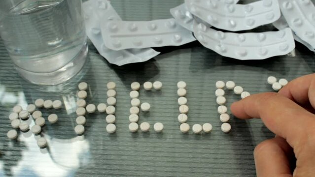 A woman with a mental disorder is about to commit suicide by poisoning herself with pills, folds the word Help from the pills. Overdose and suicide concept, suicide help. Pills on female hands.