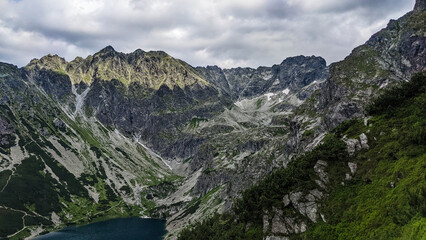 Obraz premium Incredible view of lakes and meadow under the mountains in the light of the sun. Beautiful landscape of lakes and mountains under the cloudy blue sky as wallpaper, poster or background. 
