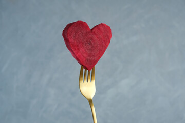 Juicy slice of raw beetroot in shape of heart on the tip of golden fork. Concept - healthy eating,...
