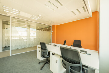Office cubicle with white furniture, black swivel chairs, plugs on the tables and glass panel as a...