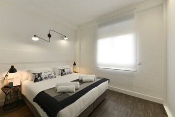Bedroom with double bed, white wooden headboard, window with blind and wooden floor